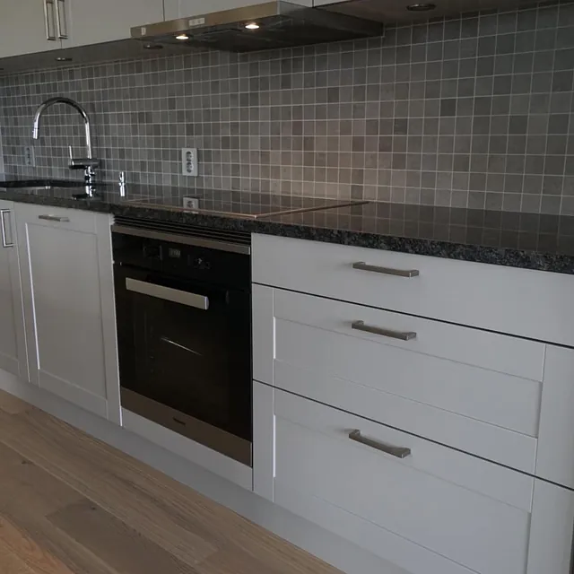 Pent kjøkken med gråbrune og beige, små fliser på veggen bak vasken